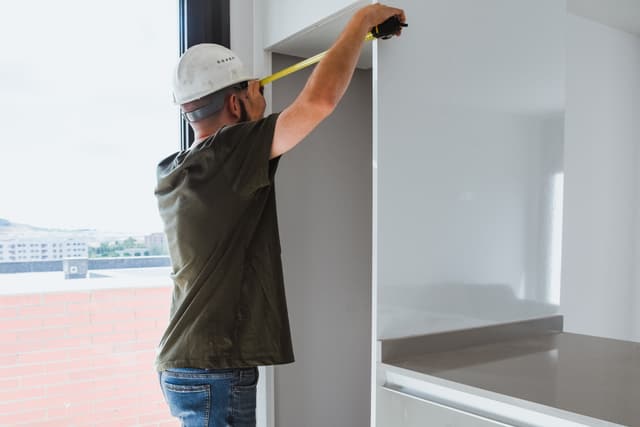 Front view of a man measuring a refrigerator cutout in a kitchen